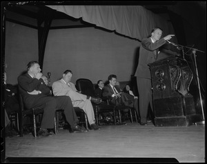 Billy Graham speaking from podium with a group of men sitting behind him