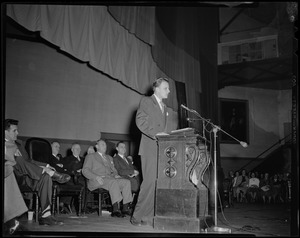 Billy Graham speaking from podium with a group of men sitting behind him