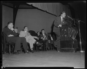 Billy Graham speaking at a podium with a group of men sitting behind him