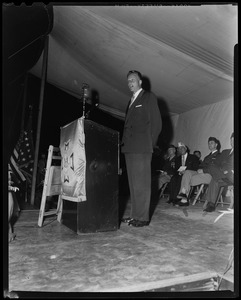Billy Graham speaking at a podium with a group of veterans seated behind him