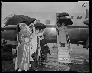 Sen. Barry Goldwater standing on stairs of American Airlines plane and waving to group while holding umbrella