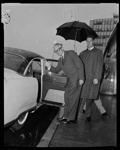 Sen. Barry Goldwater waving and getting into a vehicle, with other man holding up umbrella