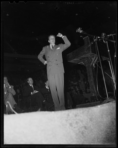 Billy Graham on stage, with left arm in the air