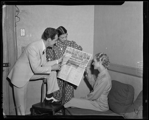 Fred Waring pointing at issue of Boston American newspaper with headline "Cronin Breaks Thumb, Sox Win" as two women look on