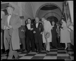 Harry Truman, in formal wear, walking arm in arm with other man, surrounded by others