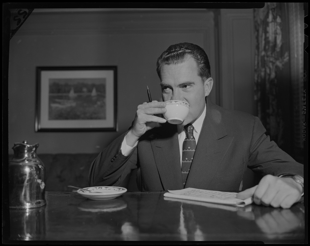 Vice President Richard Nixon, seated with pen and notepad, drinking from cup