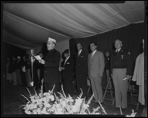 Man leading crowd in song, with Billy Graham and Richard Nixon behind him