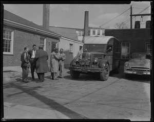 Five men standing beside armored truck, two of them looking at notepad