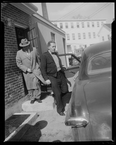 One man getting into a car, possibly armored car guard Joe Riley, as another man exits a doorway
