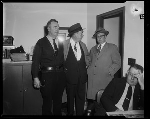 Three men standing behind man seated with hand on his forehead