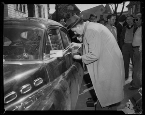 Two men dusting door handle of car with onlookers nearby