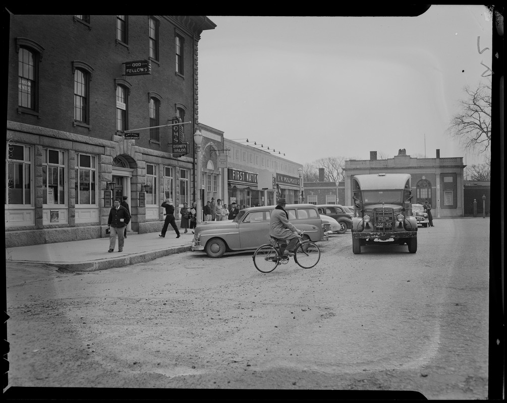 View of pedestrians, bicyclist, cars, and stores on a street