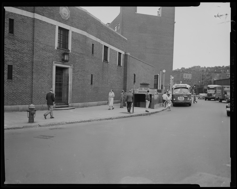 Street scene with pedestrians and vehicles near underpass entrance, outside Charles Street Jail