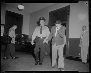 Police officer escorting handcuffed Elmer "Trigger" Burke, who is covering his face with his hand