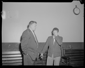 Man handcuffed to Elmer Burke, who is covering his face with his left hand