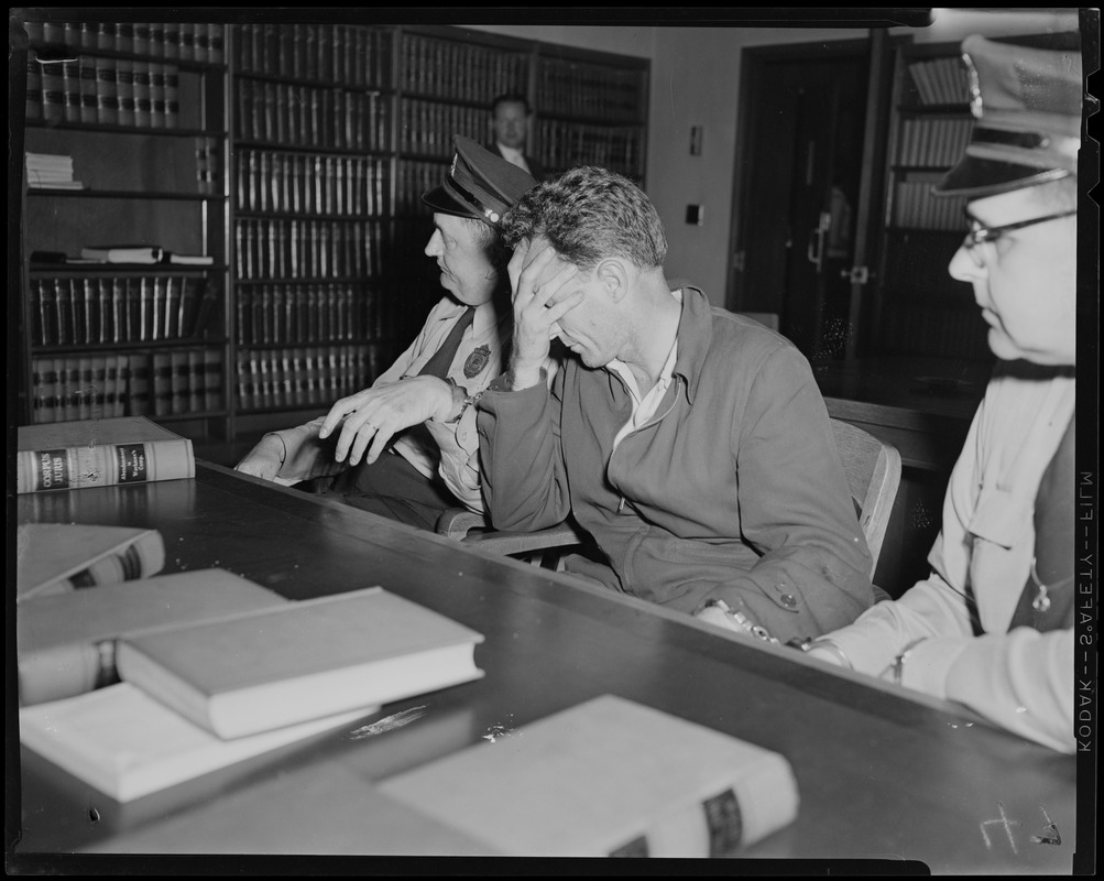 Elmer Burke with head in hands, seated between two officers