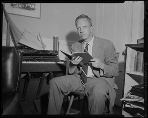 Man seated near piano, holding book