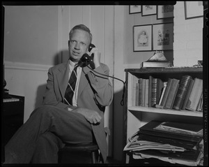 Man seated next to bookshelf, on telephone