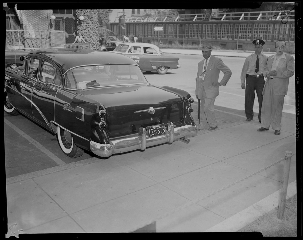 Police officer, man holding rifle, and man holding notepad next to car with Boston Police car nearby