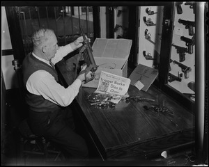 Police Det Earl L. Laird Ballistion at Headquarters is shown as he puts away Trigger Burke's arsenal of firearms which will eventually be destroyed because his case is closed...as shown by the news headlines