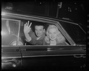 Carroll (Baby Doll) Baker shown in car outside South Station, waves to fans. Left, Bob DeSemone, City of Boston greeter