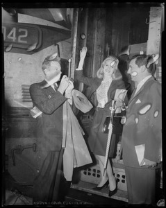 Carroll Baker waves from train steps at South Station, with City of Boston greeter Bob DeSemone and photographer