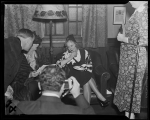 Sonja Henie seated, in conversation with others and holding plate
