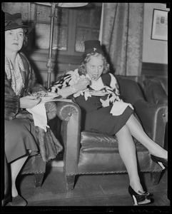 Sonja Henie seated with another woman, eating