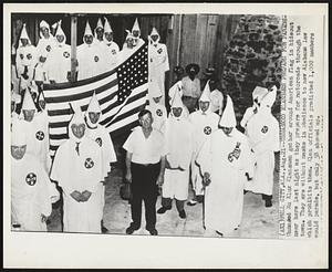 Unmasked Klansmen Prepare for Parade-Unmasked Ku Klux Klansmen gather around American flag in hideout near here last night as they prepare for motorcade through the town. They are without masks in obedience to new Alabama law which prohibits them. Klan officials predicted 1,000 members would parade, but only 58 showed up.