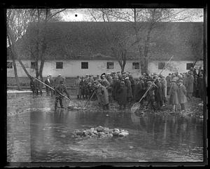 A group of people, including photographers, looking at items pulled out of a pond in a net