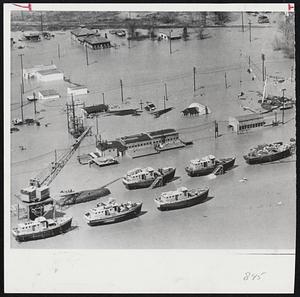 Launching Almost Premature-These tugboats, under construction at the Missouri Valley Steel Shipyards at Leavenworth, Kas., can now await their normal launching as the floodwaters at the Missouri river, just short of the bottom of their hulls, starts to recede. Men in a boat (under crane, left) keep a check on the valuable boats and equipment as the water stands at window-level on the houses in the area.