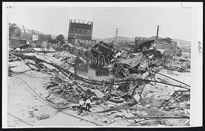 Waterbury-Wreckage of New Haven Railroad bridge dwarfs rescue workers wearing protective face masks. Demolished tenement is at right. Splintered freight cars and twisted rails mingle.