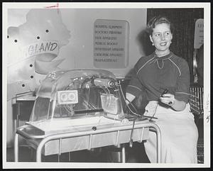 Traveling Incubator-Latest device for carrying premature or ailing infants from one hospital to another for treatment is this portable incubator which can be plugged into cigarette lighter socket in automobile. Grace Barr of Attleboro examines is.
