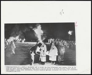 Klansmen Get a Light--Ku Klux Klansmen, and women, file by to pick up their burning torches as they form a circle around a 30-foot burning cross during last night's rally near Salisbury. Several hundred persons attended the rally.