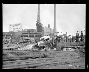 People stand beside a car that has gone off the road, Domino Sugars factory in background