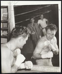 Through the Looking Glass-Lee Savold, heavyweight contender, is shown shadowboxing while in training at St. Louis. The mirror reflects all the characters needed for a successful future. Behind Savold's reflection stand the reflections of his manager, Pinky George (left), and Trainer Eddie Meyer.