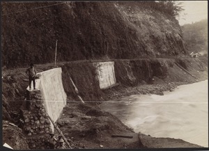 Man standing on retaining wall on edge of railroad tracks near Revetazón River; heads of 3 men on left in foreground