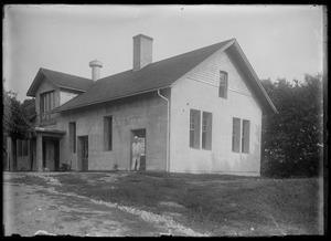 House with attached shed. Adult male figure standing in doorway