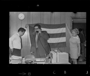 While one demonstrator calls friends to tell of the latest developments, two other members of the Spanish speaking community hang up a Puerto Rican flag in the ABCD office on Tremont St. after seizing the office