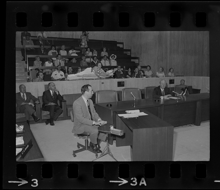 Former Boston John F. Collins addresses City Council hearing on the plight of handicapped persons as Helene Cummings watches from her stretcher-bed