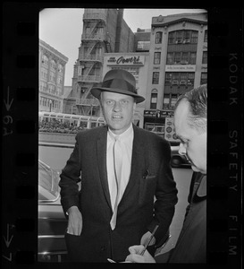Billy Graham with hat on outside of Hotel Statler Hilton in Boston speaking with a reporter