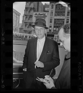 Billy Graham with hat on outside of Hotel Statler Hilton in Boston speaking with a reporter