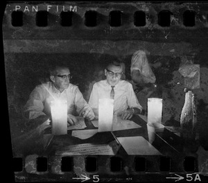 Two men sitting at table talking and reading by candlelight during Boston blackout
