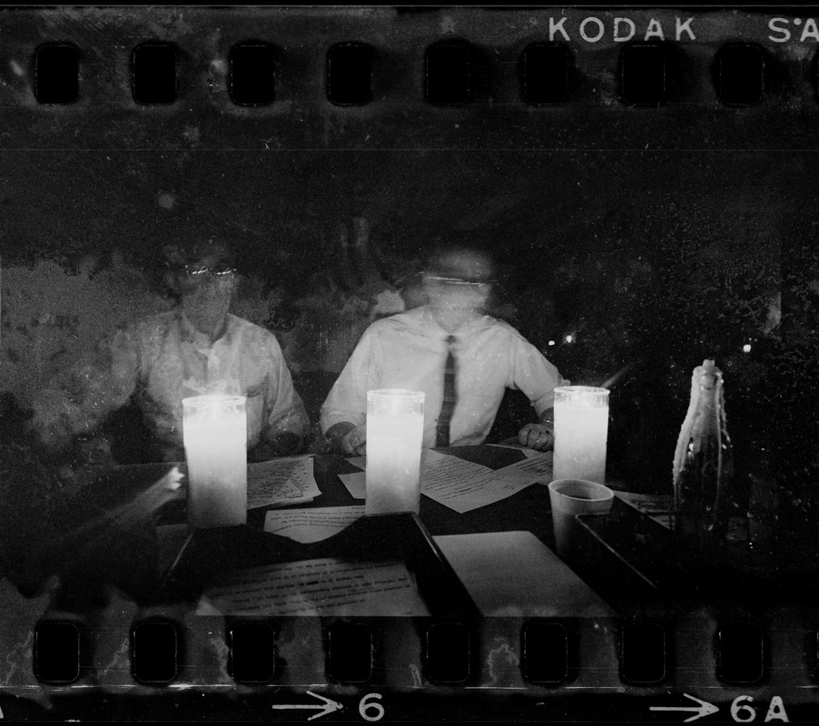 Two men sitting at table talking and reading by candlelight during Boston blackout