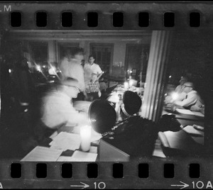People at desks in a large office lit by candlelight and a portable emergency light during Boston blackout