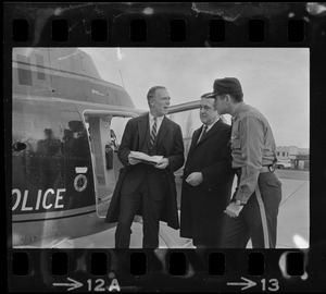 Boston Mayor Kevin White speaking with a state policeman and another man while standing next to a police helicopter