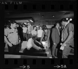 Mayor Kevin White seated and tying his shoes while others look on at Lucky Strike Alley