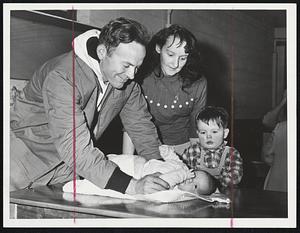 Dressing The Baby on a cafeteria table at Hull’s Memorial School are Mr. and Mrs. William Coulter of 79 Kenberma St. and two-year-old David. Baby’s bottle and a few diapers were all they had a chance to grab before being rescued by a Coast Guard amphibious craft yesterday afternoon.