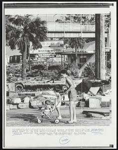 Billoxi, Miss.: A young mother strolls her baby down what used to be the main highway through this resort town. Hurricane Camille reduced the motels in the background to ruble.