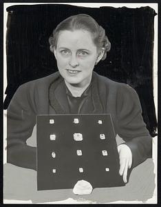 Miss Gladys Hannaford holds a tray containing 12 small diamonds cut from the huge 726 carat Jonkers diamond, a replica of which rests in front of the tray. The cut stones weigh only 375 carats, the cutting and polishing process having absorbed the lost weight. Total value of the stones is $2,000,000.